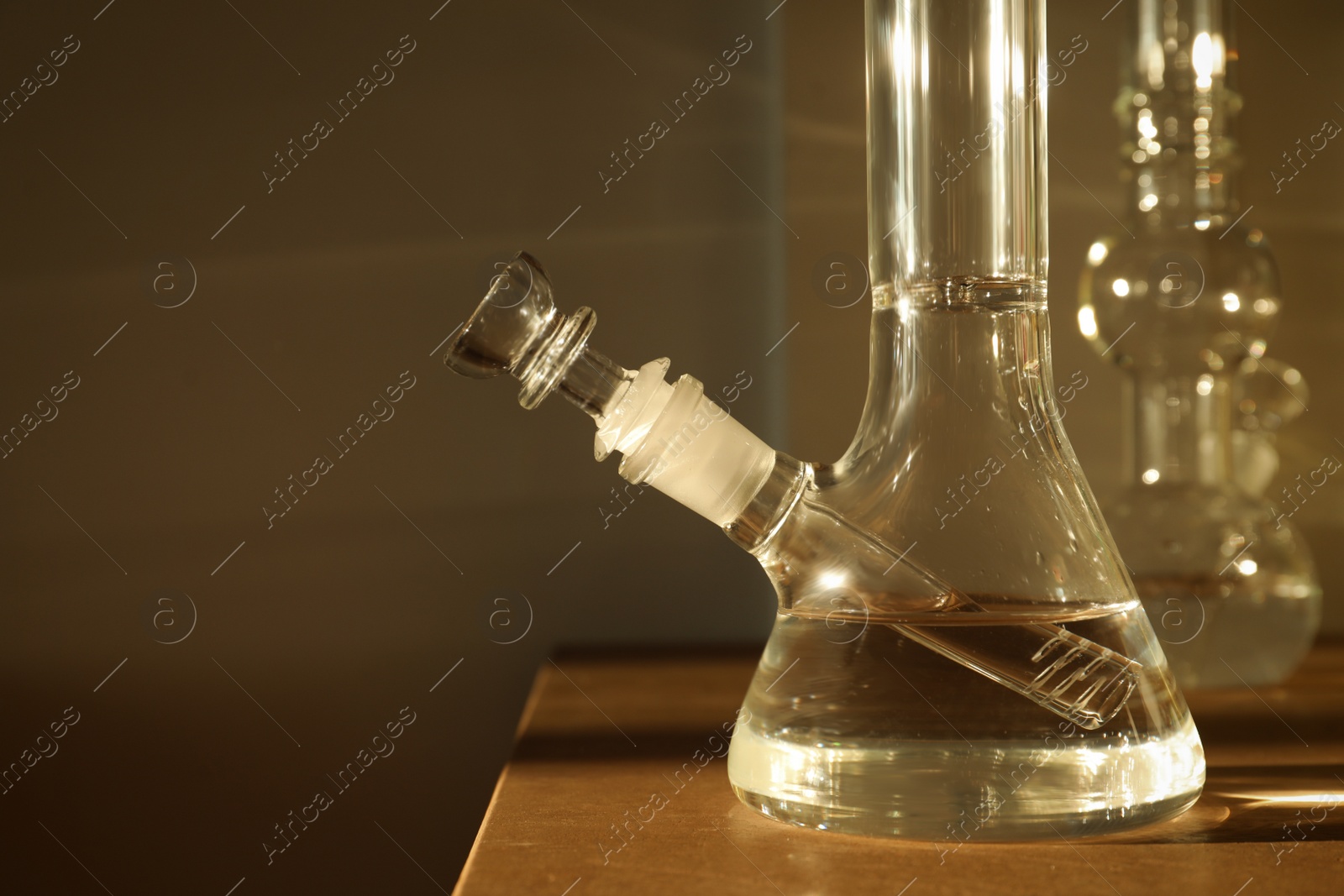 Photo of Closeup view of glass bong on wooden table indoors. Smoking device