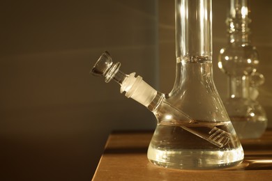 Photo of Closeup view of glass bong on wooden table indoors. Smoking device