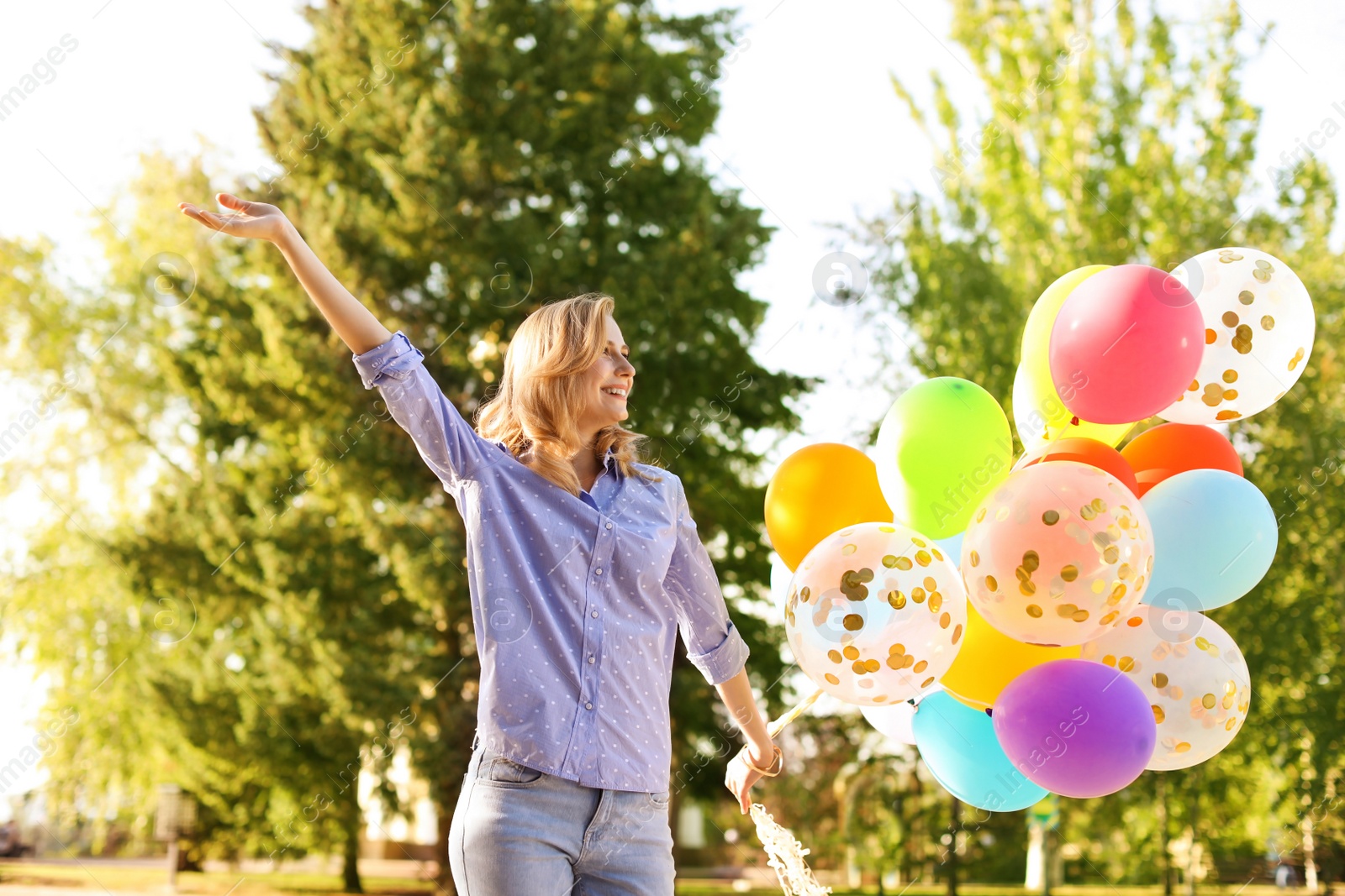 Photo of Young woman with colorful balloons outdoors on sunny day