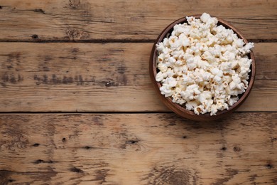 Photo of Bowl of tasty popcorn on wooden table, above view. Space for text