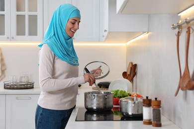 Photo of Muslim woman cooking dish in saucepan on cooktop indoors