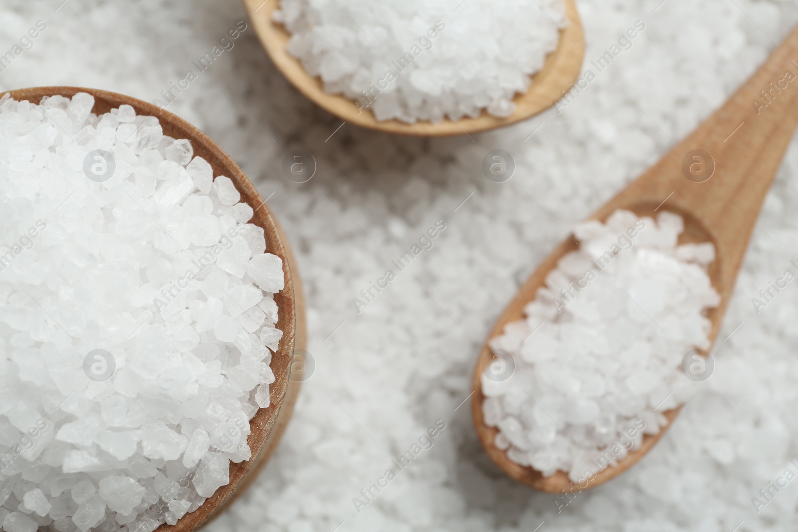 Photo of Pile of natural sea salt with wooden bowl and spoons, flat lay