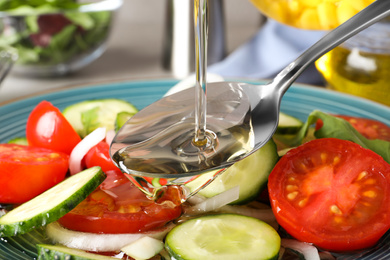 Photo of Adding cooking oil to delicious salad on table, closeup