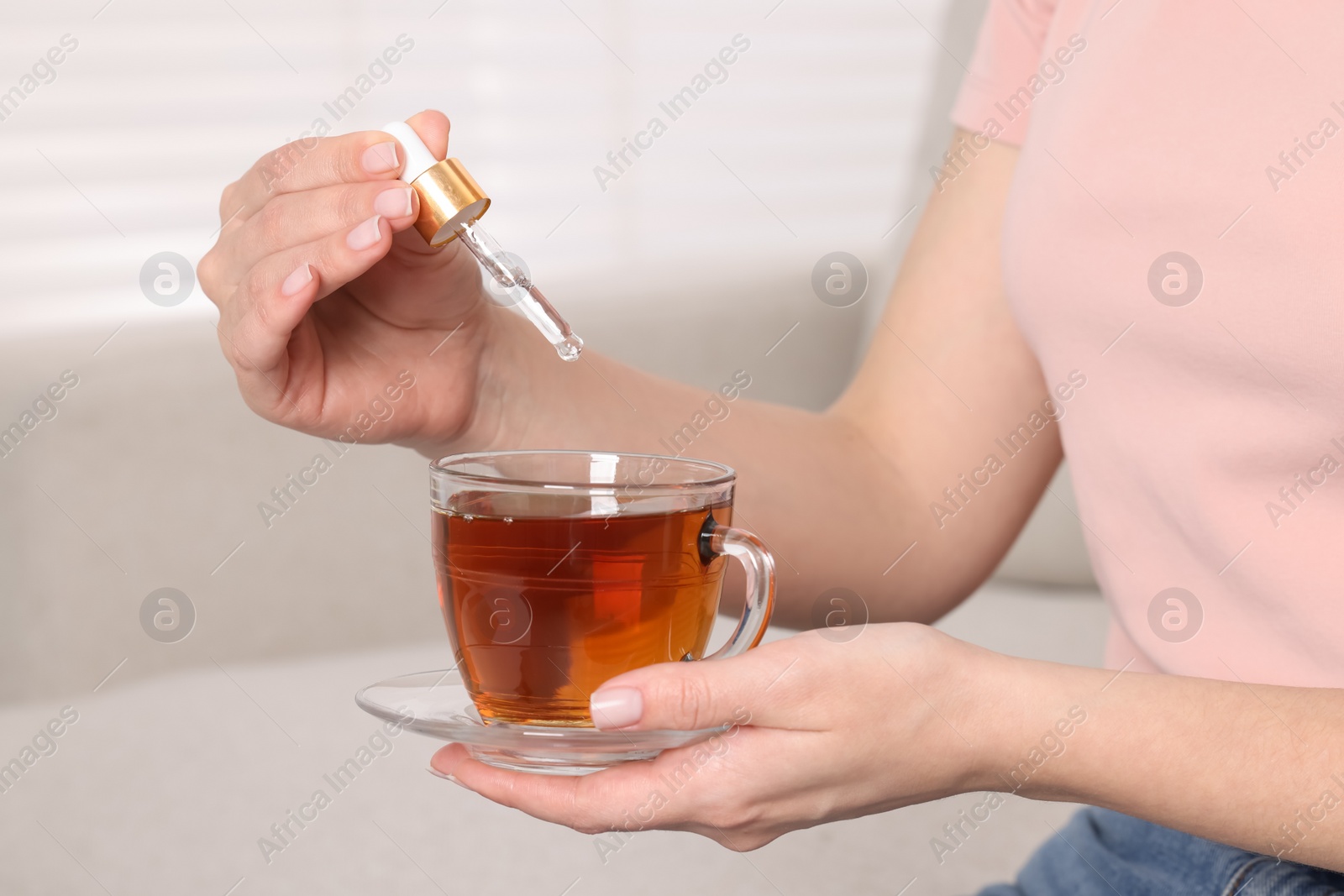 Photo of Woman dripping food supplement into cup of tea indoors, closeup