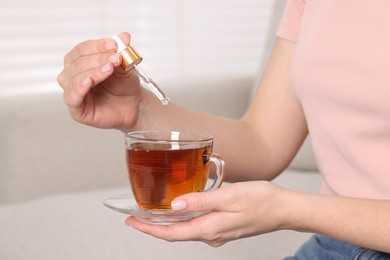 Photo of Woman dripping food supplement into cup of tea indoors, closeup