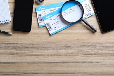 Photo of Flat lay composition with avia tickets and magnifying glass on wooden table, space for text. Travel agency concept