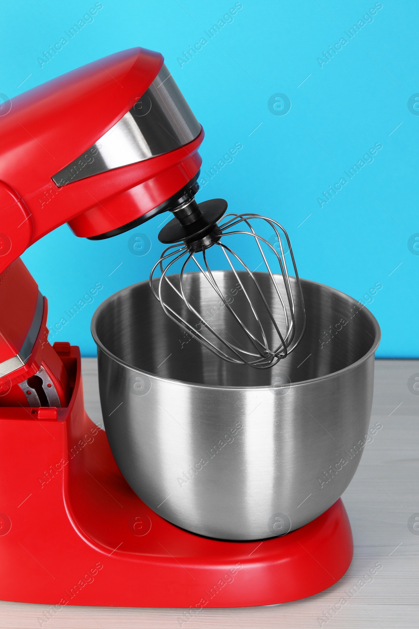 Photo of Modern red stand mixer on white wooden table against turquoise background