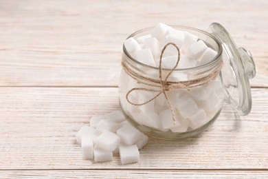 Photo of Glass jar of refined sugar cubes on light wooden table