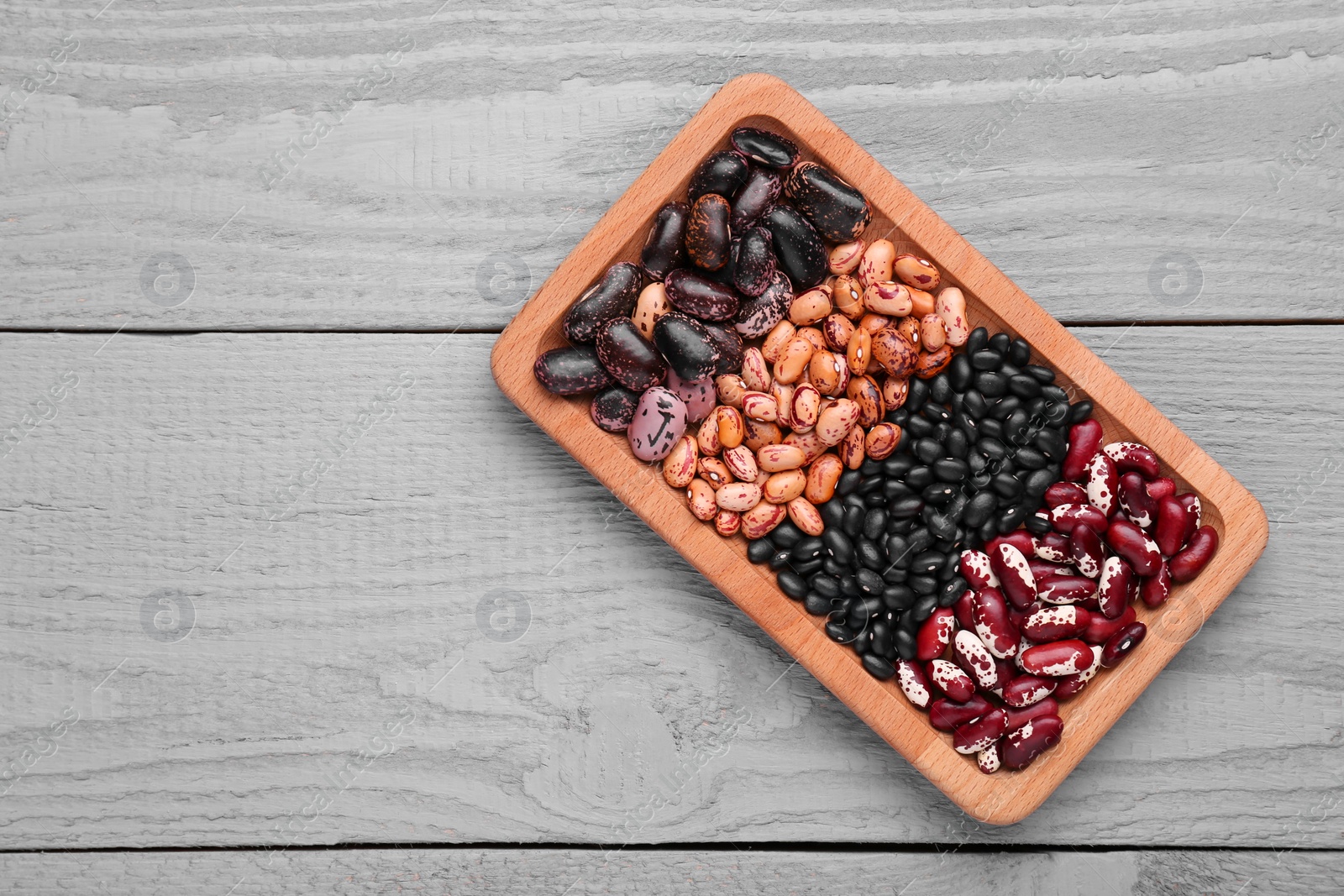 Photo of Plate with different kinds of dry kidney beans on light grey wooden table, top view. Space for text