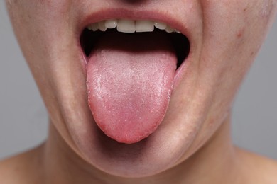 Woman showing her tongue on grey background, closeup