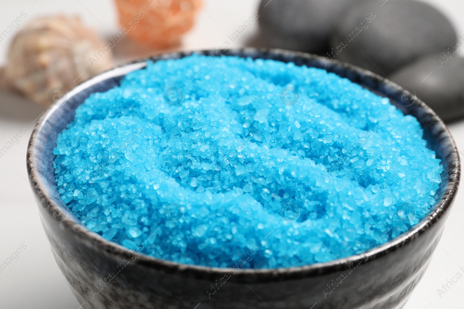 Photo of Light blue sea salt in bowl on white table, closeup
