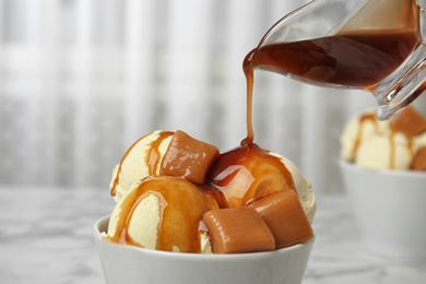 Pouring caramel sauce onto delicious ice cream in bowl on table, closeup. Space for text