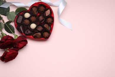 Photo of Heart shaped box with delicious chocolate candies, roses and ribbon on pink background, flat lay. Space for text