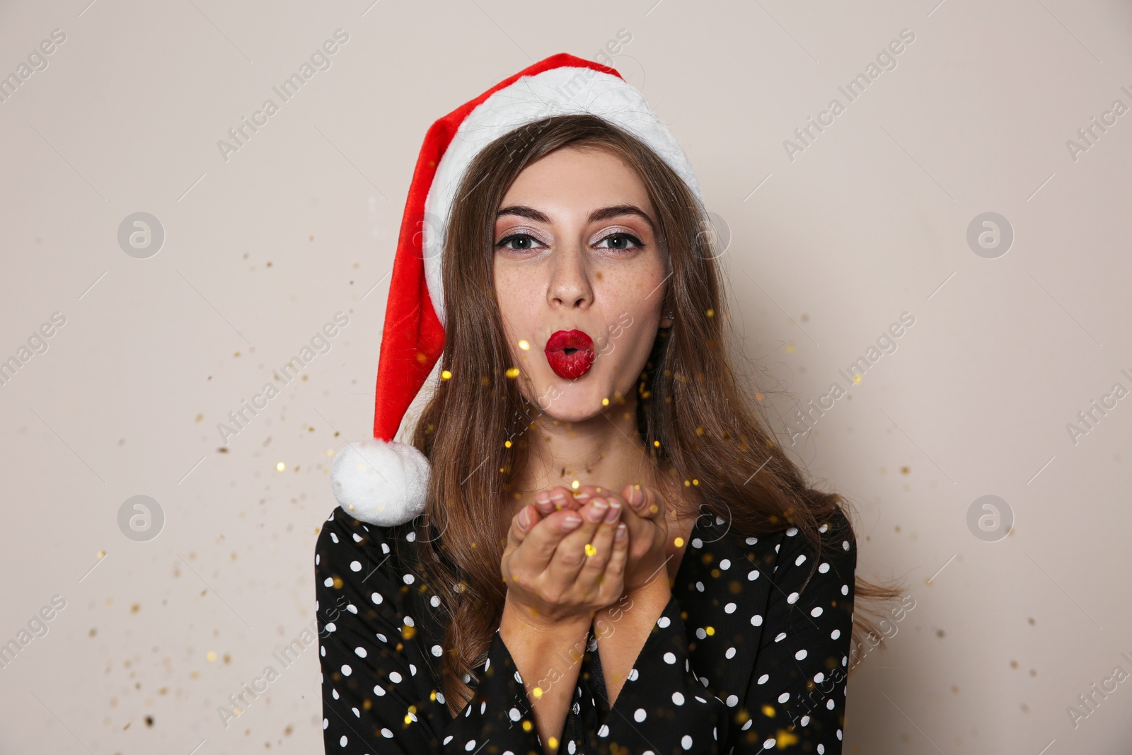 Photo of Beautiful woman in Santa hat blowing glitter on beige background. Christmas party
