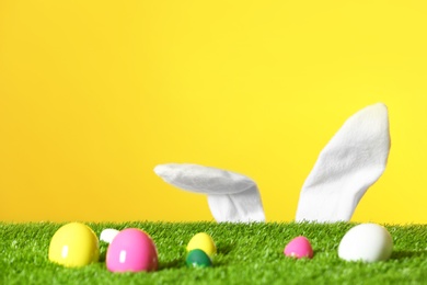 Photo of Easter eggs on green lawn and funny bunny ears against color background, space for text