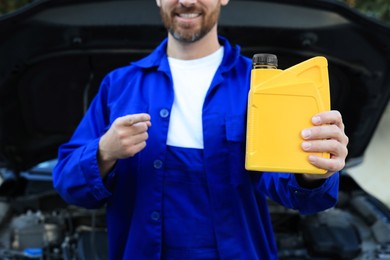Photo of Worker pointing at yellow container of motor oil near car outdoors, closeup