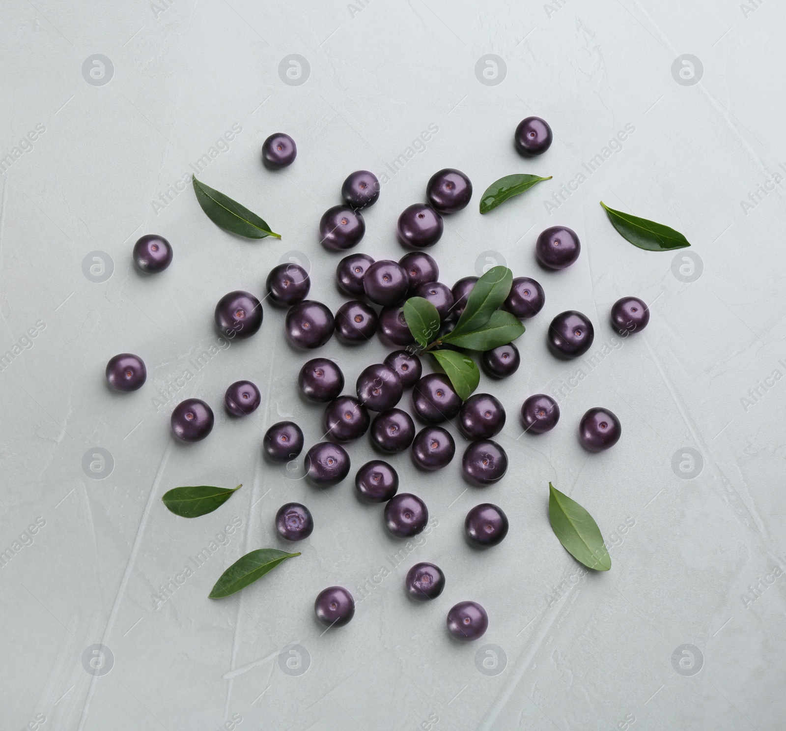 Photo of Fresh acai berries and green leaves on light grey table, flat lay