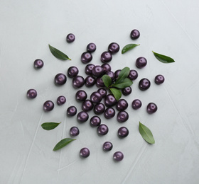 Fresh acai berries and green leaves on light grey table, flat lay