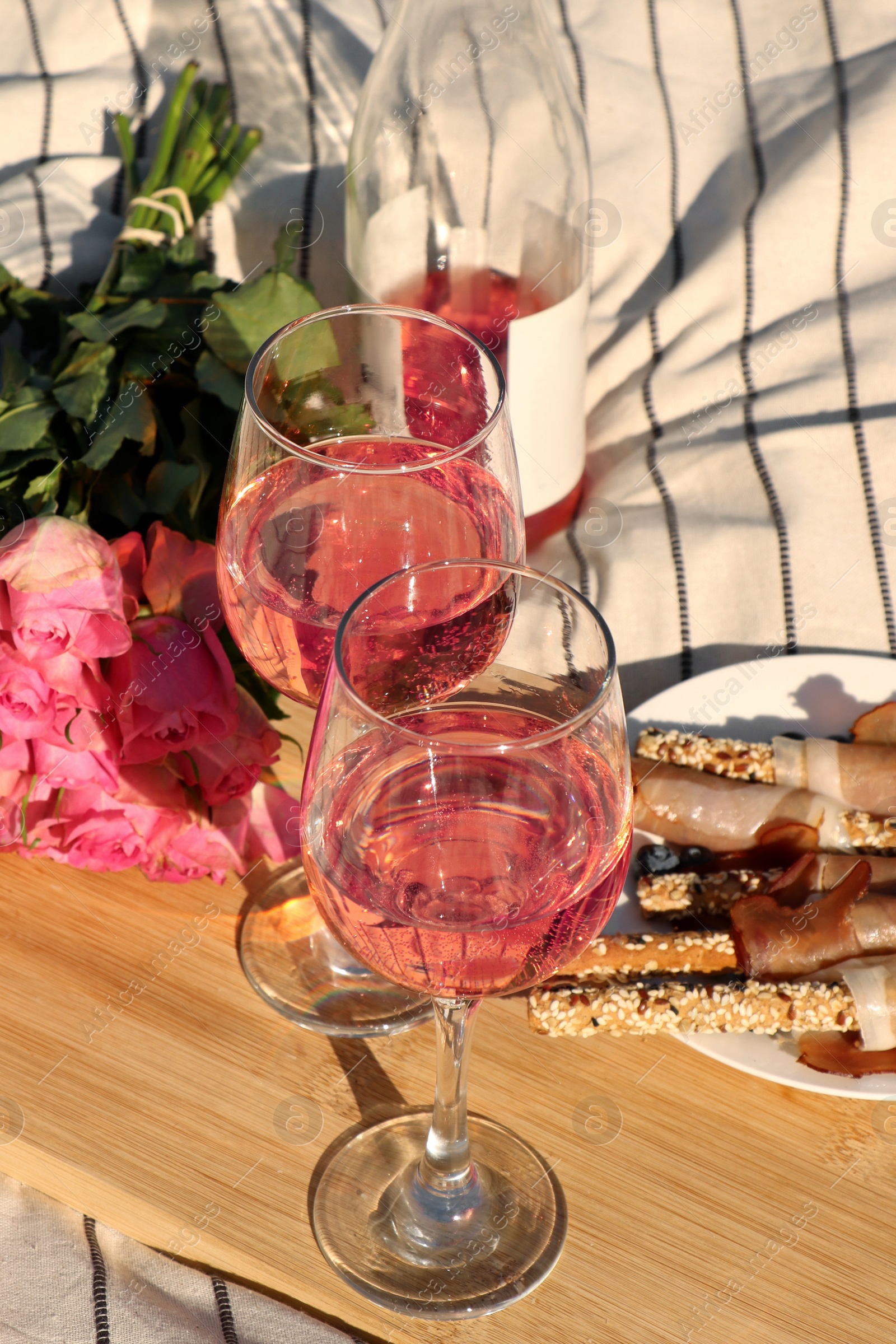 Photo of Glasses of delicious rose wine, flowers and food on white picnic blanket