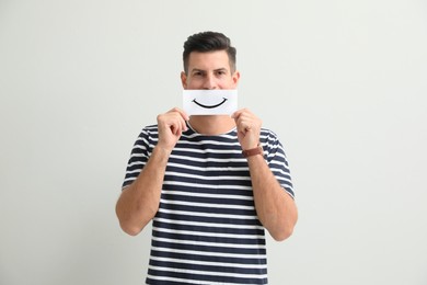 Photo of Man hiding emotions using card with drawn smile on white background