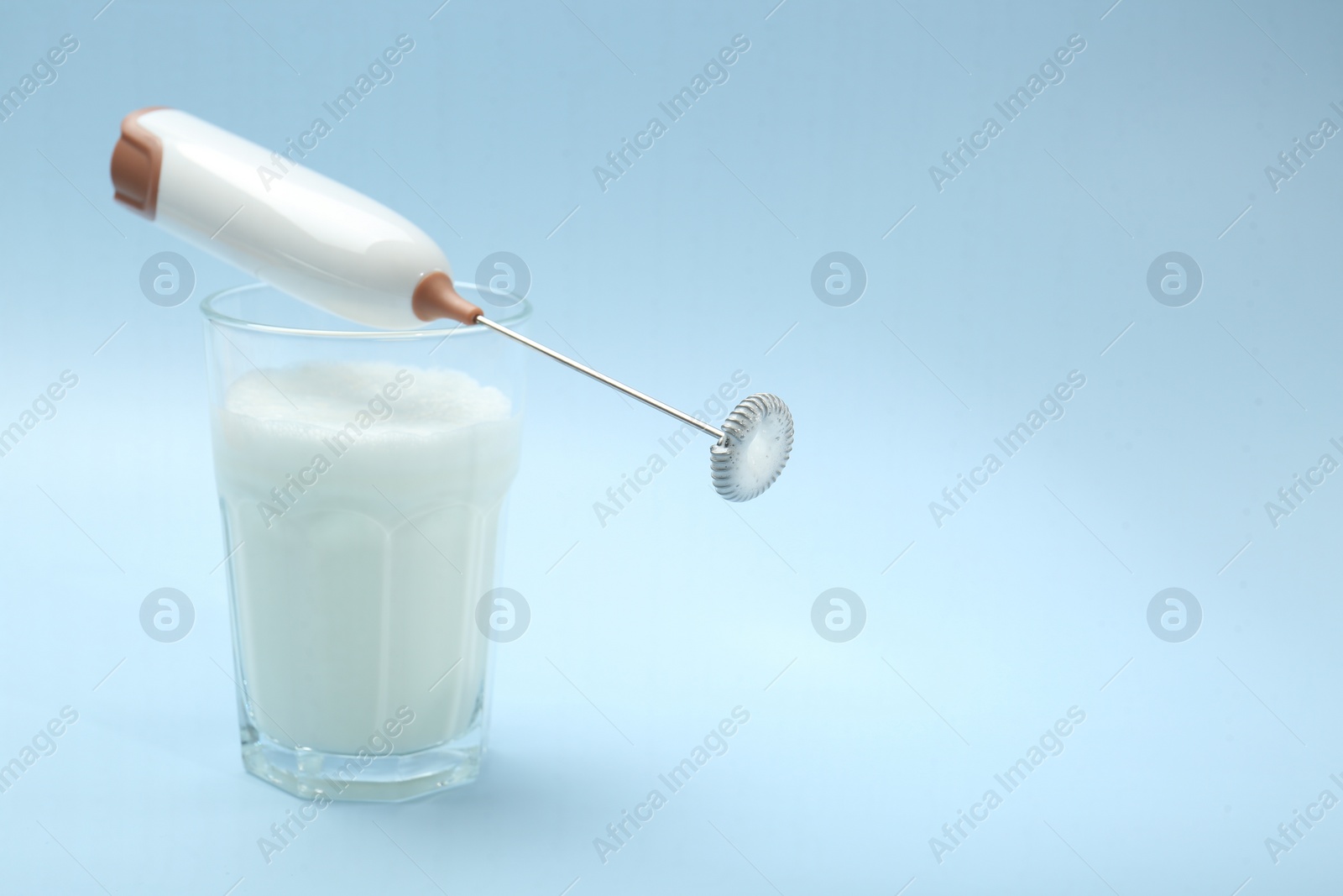 Photo of Mini mixer (milk frother) and whipped milk in glass on light blue background. Space for text