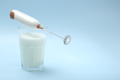 Mini mixer (milk frother) and whipped milk in glass on light blue background. Space for text