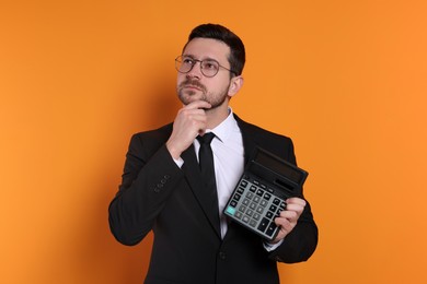 Photo of Thoughtful accountant with calculator on orange background