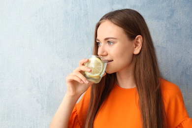Young woman drinking lemon water on color background