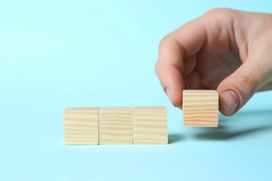 Photo of Woman arranging cubes on light blue background, closeup with space for text. Idea concept