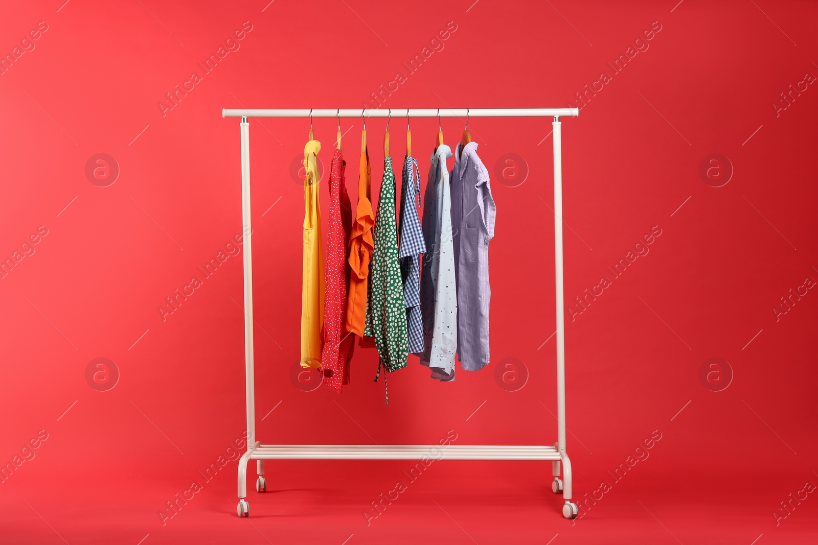 Photo of Bright clothes hanging on rack against red background. Rainbow colors