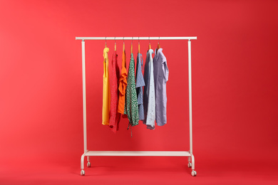 Photo of Bright clothes hanging on rack against red background. Rainbow colors