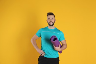 Handsome man with yoga mat on yellow background