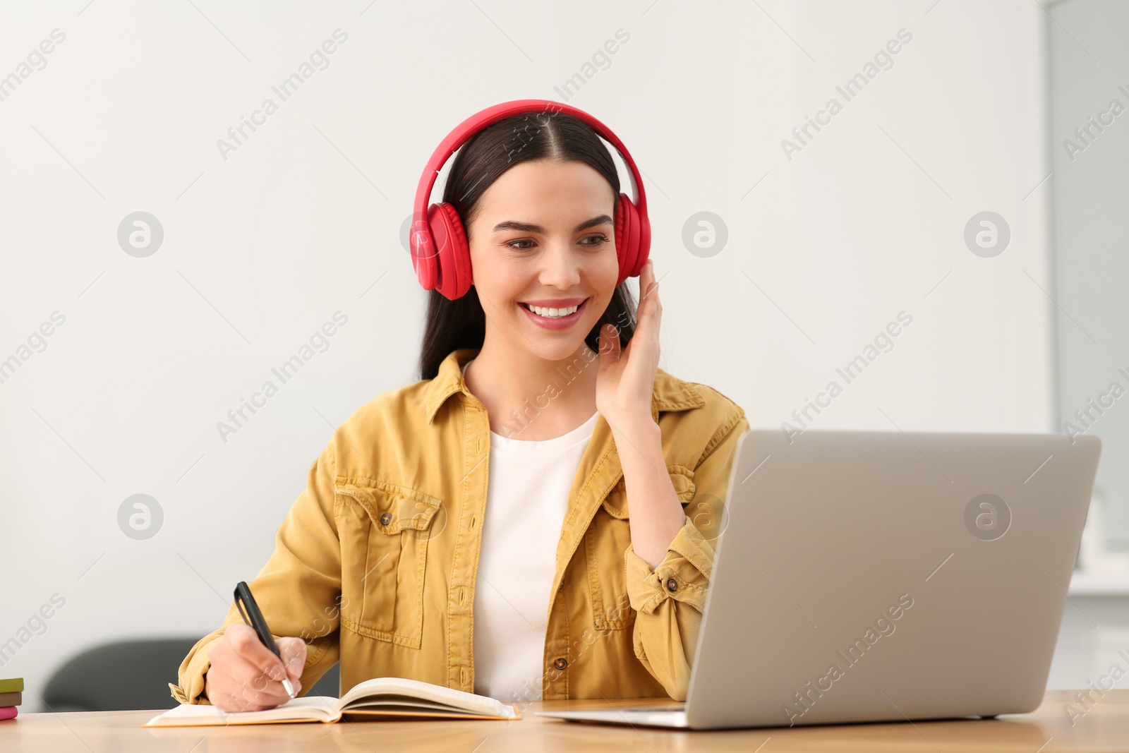 Photo of Online translation course. Student in headphones writing near laptop at home