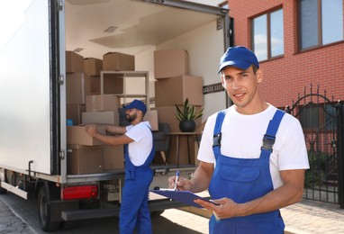 Photo of Moving service workers outdoors, unloading boxes and checking list