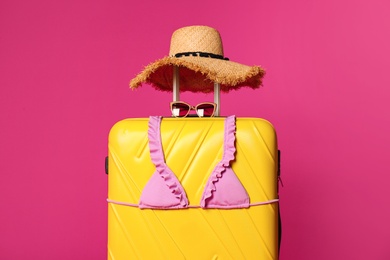 Stylish suitcase with hat, sunglasses and bikini top on color background