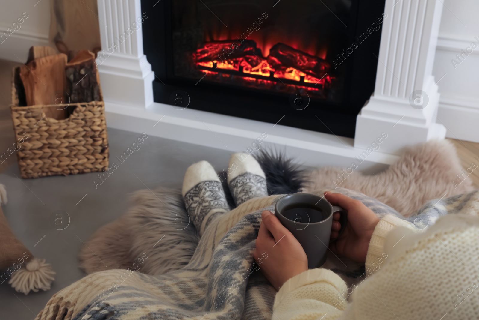 Photo of Woman with cup near fireplace indoors, closeup. Cozy atmosphere