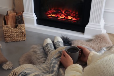 Woman with cup near fireplace indoors, closeup. Cozy atmosphere