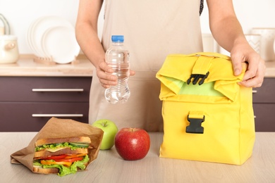 Photo of Woman packing food for her child at table in kitchen, closeup. Healthy school lunch