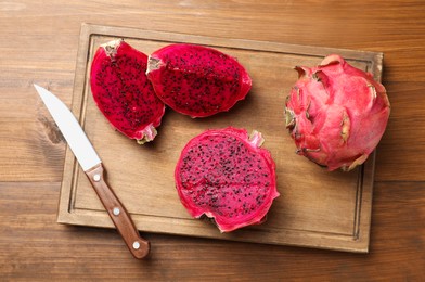 Photo of Board with delicious red pitahaya fruits and knife on wooden table, top view