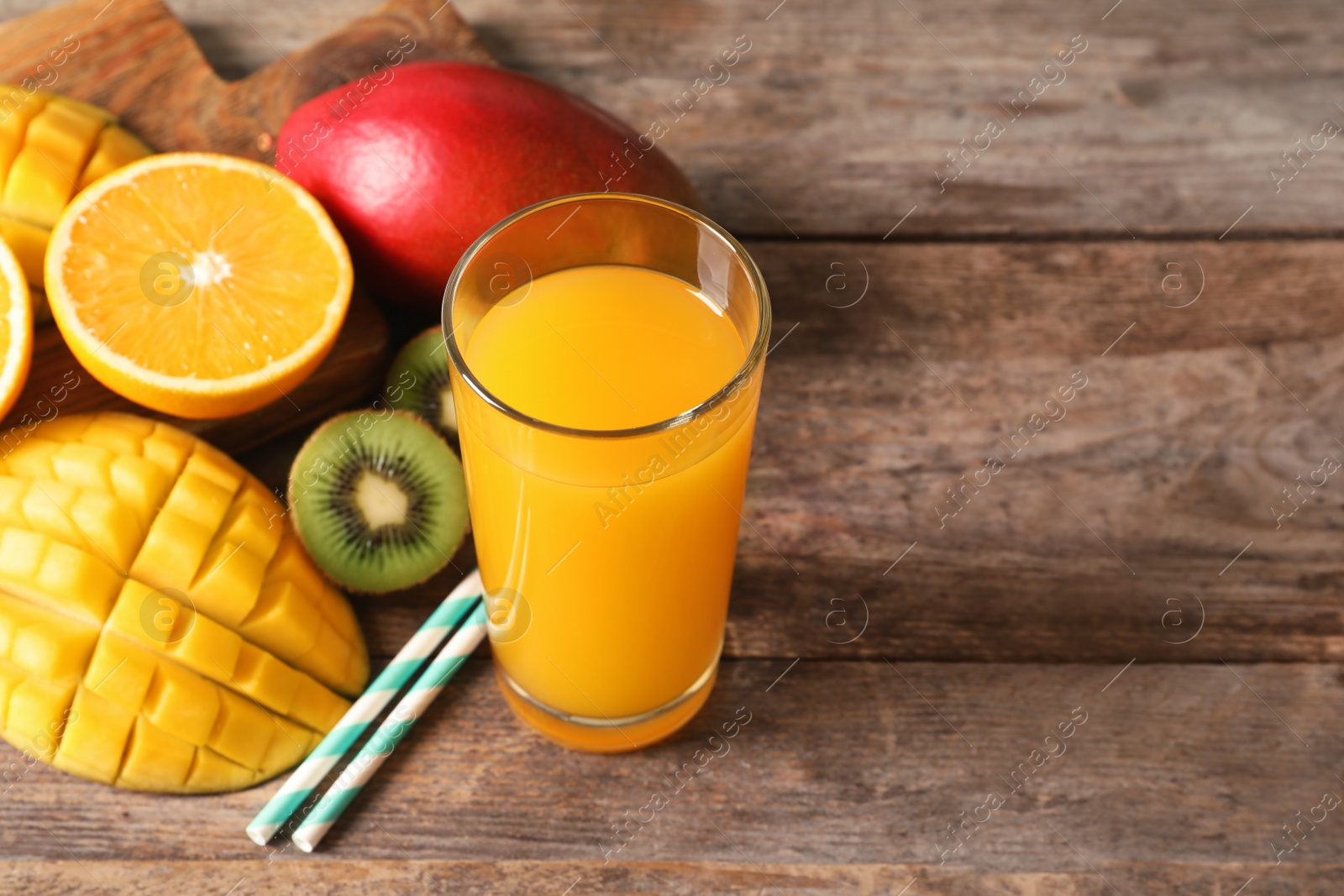 Photo of Tasty tropical drink with mango and fresh fruits on wooden table. Space for text