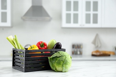 Different fresh vegetables in crate on white kitchen table. Space for text