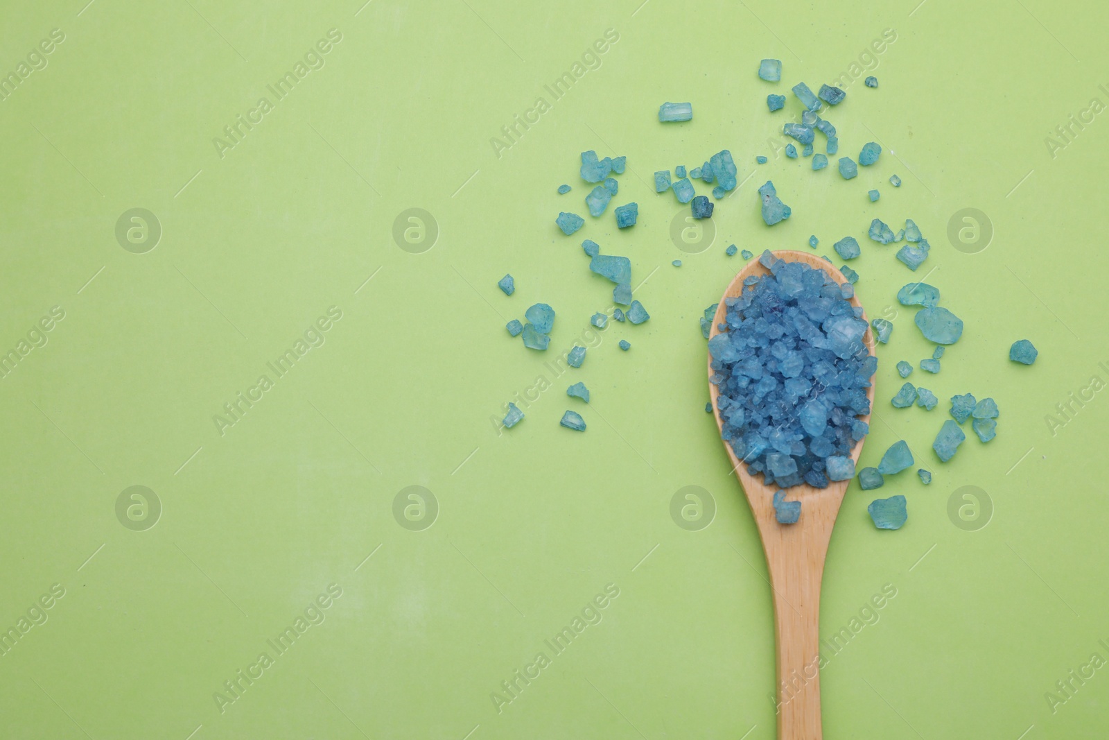 Photo of Spoon with blue sea salt on light green background, top view. Space for text