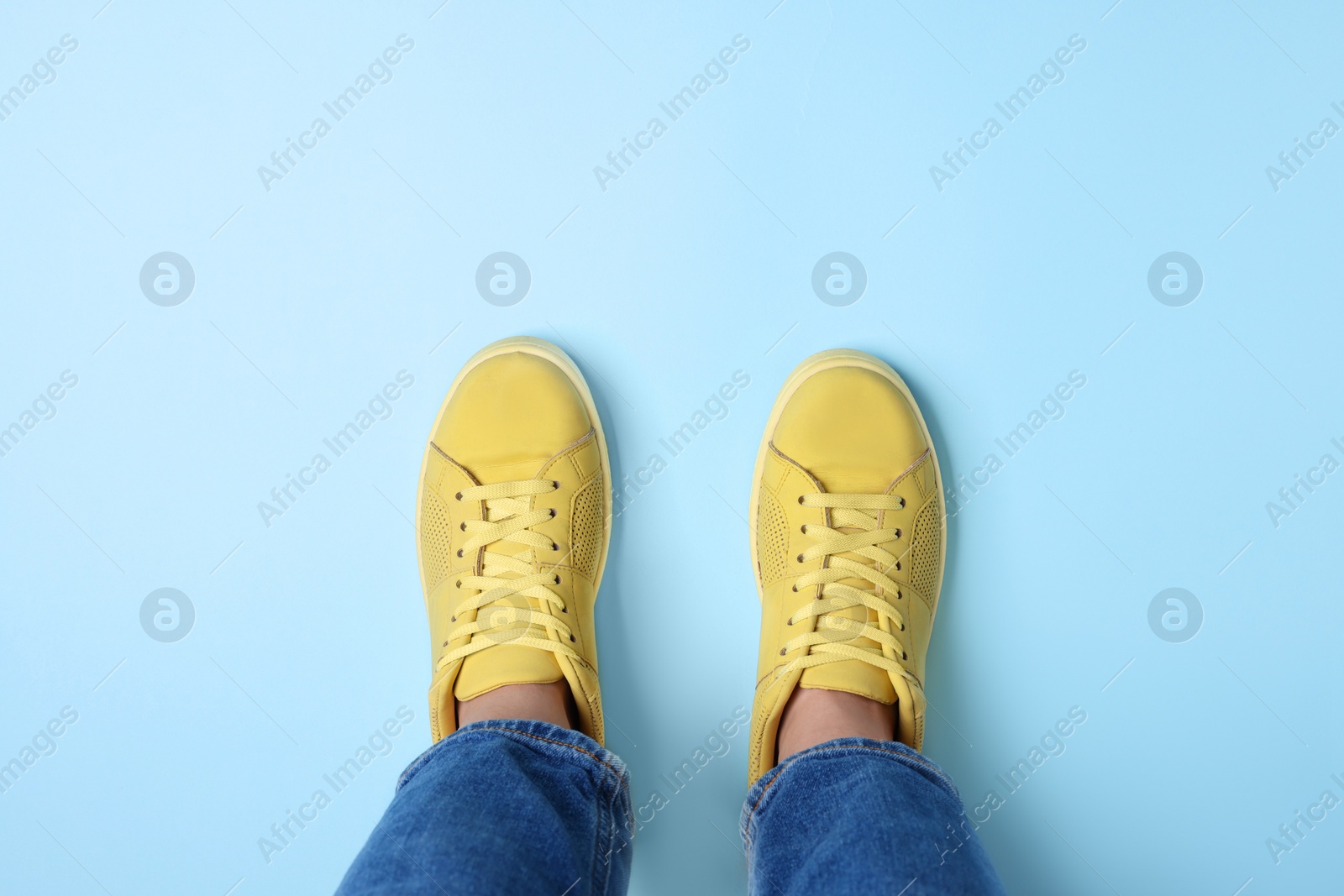 Photo of Woman in stylish sneakers on light blue background, top view