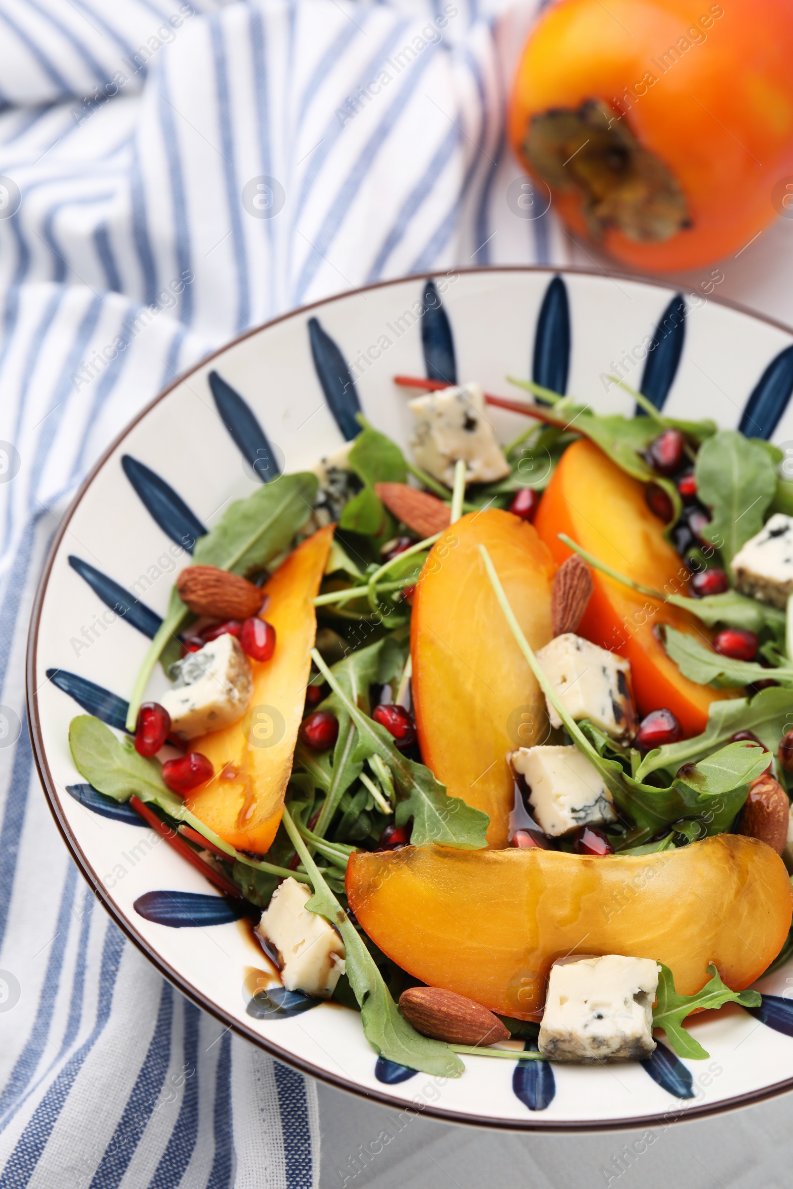 Photo of Tasty salad with persimmon, blue cheese, pomegranate and almonds served on white tiled table, closeup
