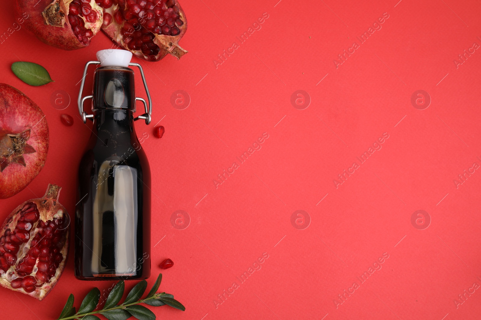 Photo of Tasty pomegranate sauce in bottle, leaves and fruits on red background, flat lay. Space for text