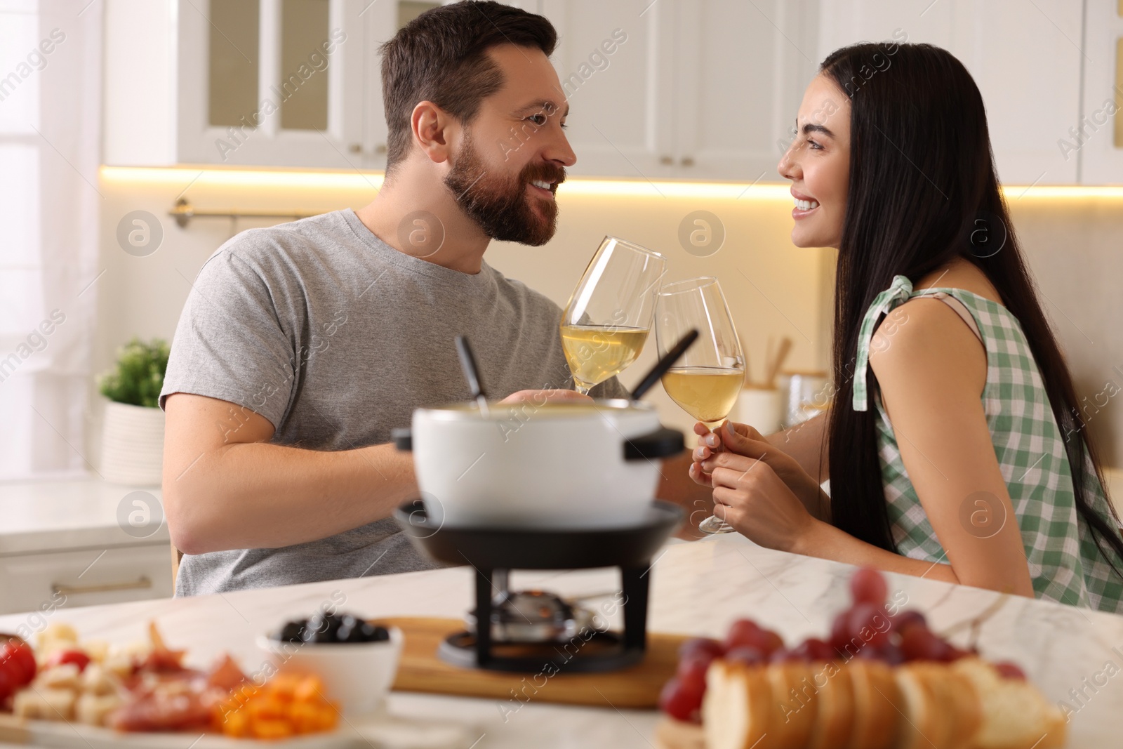 Photo of Romantic date with fondue. Couple clinking glasses of wine at home