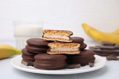 Photo of Tasty banana choco pies and pieces of chocolate on white table, closeup