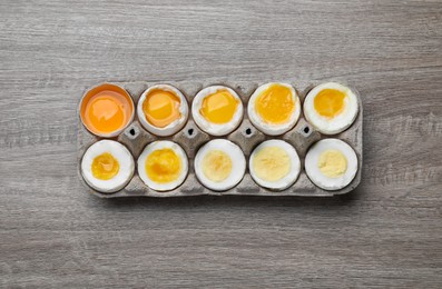 Photo of Boiled chicken eggs of different readiness stages in carton on wooden table, top view