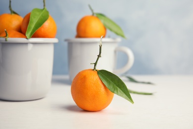 Fresh ripe tangerines with green leaves and mugs on table