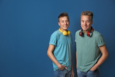 Teenage twin brothers with headphones on color background. Space for text